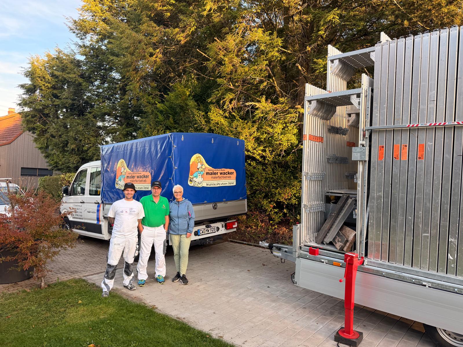 Drei Personen vom Malerfachbetrieb Wacker stehen vor beschriftetem Firmenfahrzeug mit Gerüstanhänger