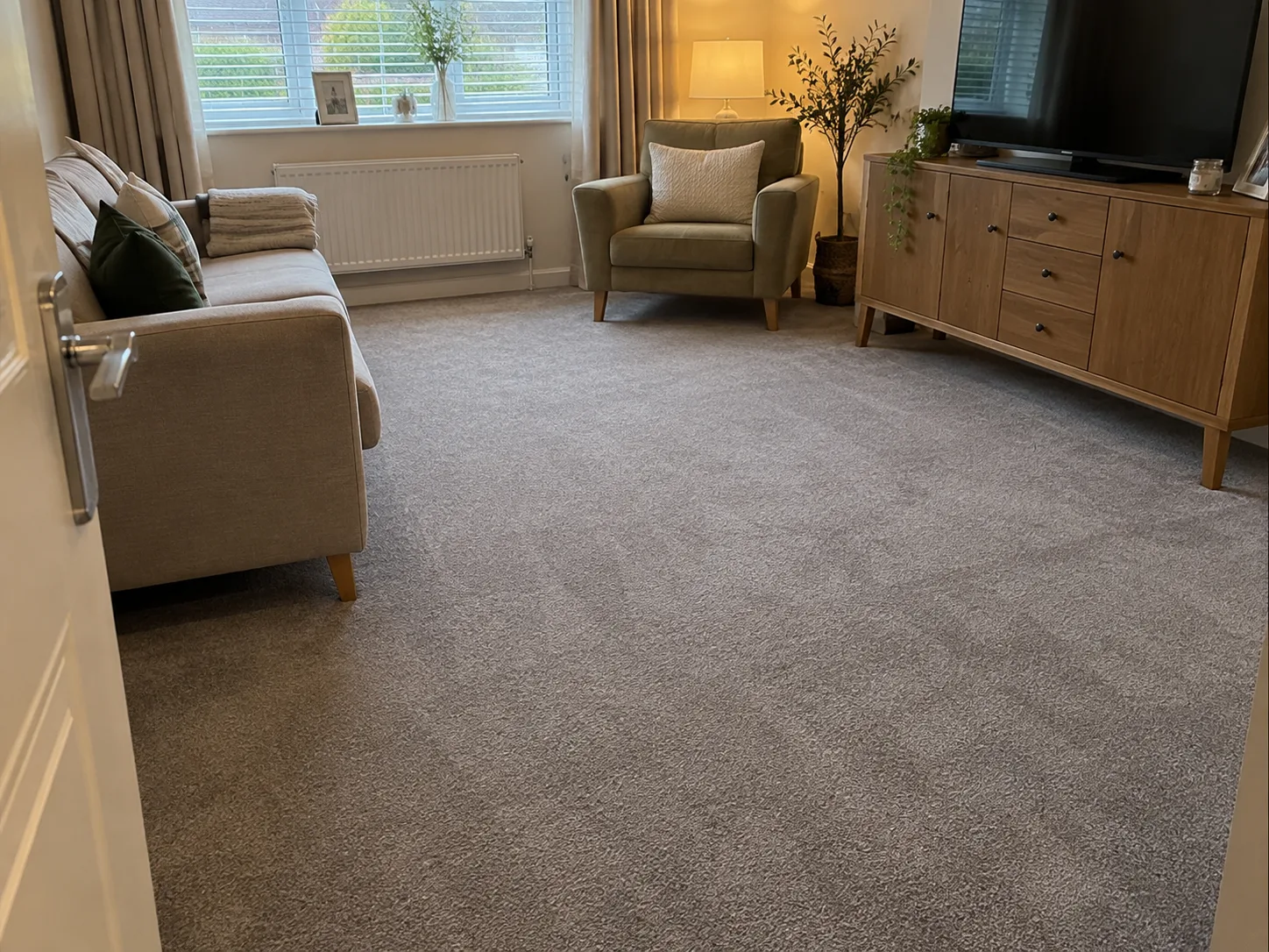 Helles Wohnzimmer mit frisch verlegtem grauem Teppich, Sofa und Sessel